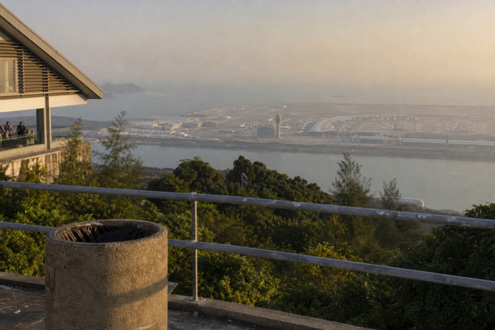 Afternoon light over the airport island and sea from a high plateau viewpoint, no text, no logos, no people
