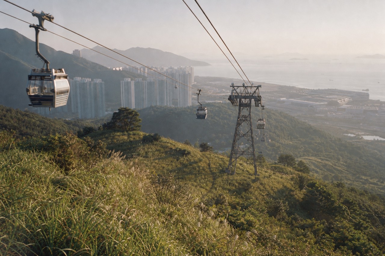 Cable car cabins crossing green Lantau hillside in clear morning light, no text, no logos, no people