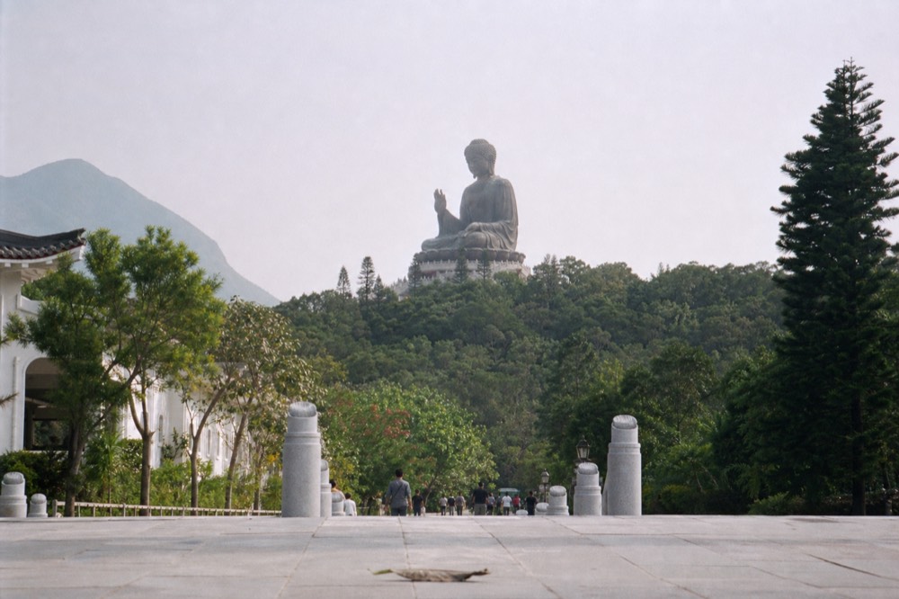The Tian Tan Buddha rising above the Ngong Ping plateau seen from the approach path, no text, no logos, no people