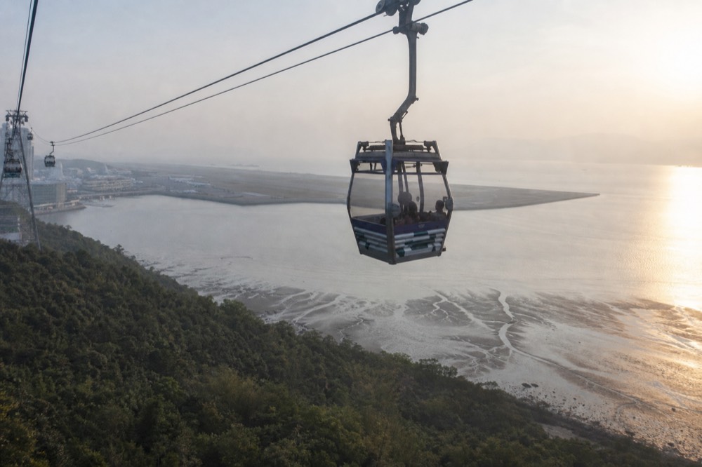 Cable car cabin crossing above Tung Chung Bay with the airport runway in the distance, no text, no logos, no people