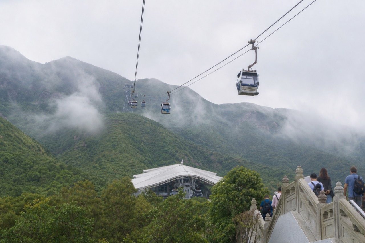 Cable car cabins travelling over green Lantau hills toward the Ngong Ping plateau, no text, no logos, no people.