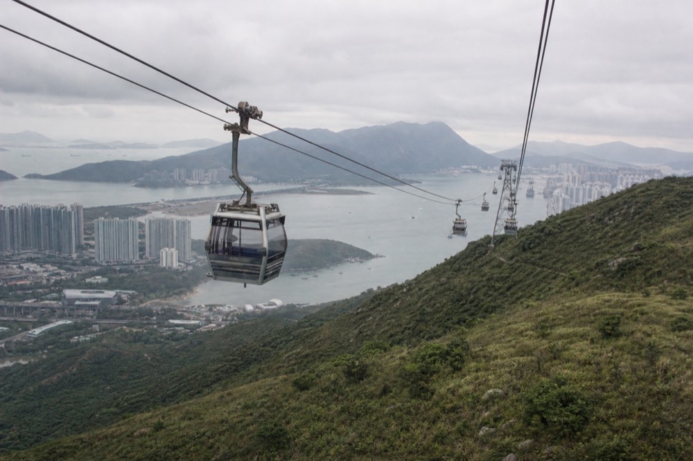 A cable car cabin crossing the green Lantau hills toward the Ngong Ping plateau, no text, no logos, no people