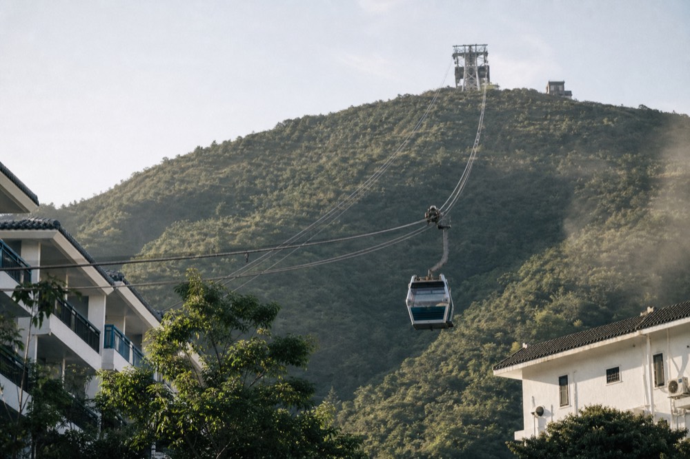 A cable car cabin crossing above green hills toward the Ngong Ping plateau, no text, no logos, no people