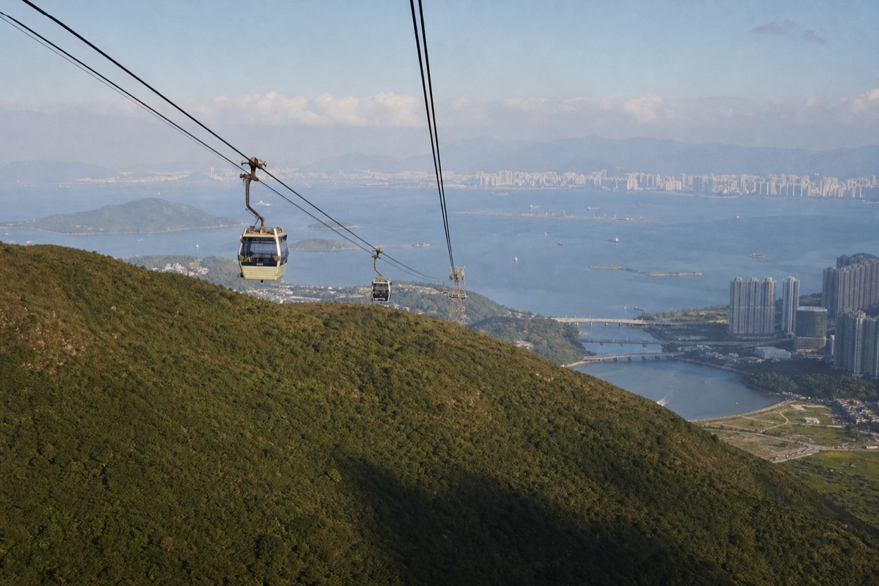 Cable car cabins crossing green hills above Lantau Island with the sea beyond, no text, no logos, no people