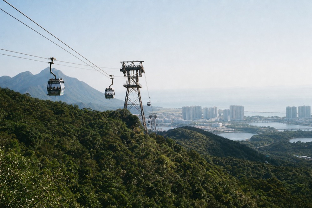 Cable car cabins travelling over forested Lantau hills toward the sea, no text, no logos, no people