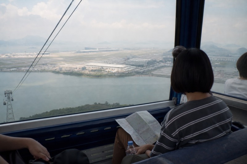 Passengers seated inside a standard Ngong Ping 360 cabin looking out over Tung Chung Bay and the airport island through large windows