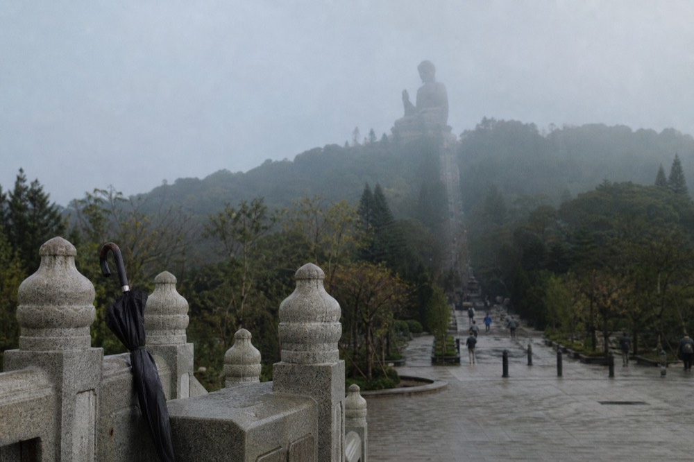 The Tian Tan Buddha seen from the approach path below the steps, green hills behind, no text, no logos, no people