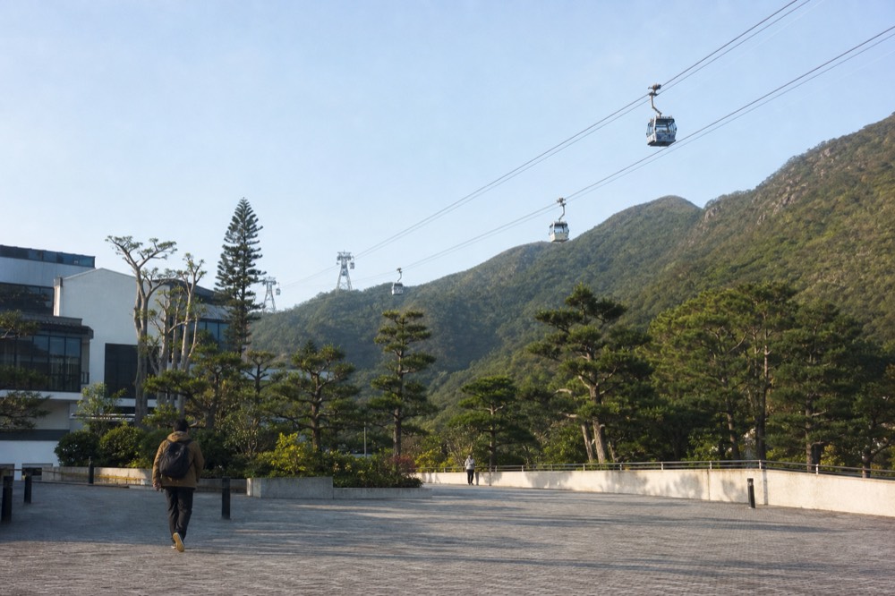 A cable car cabin travelling above green slopes towards the Ngong Ping plateau, no text, no logos, no people