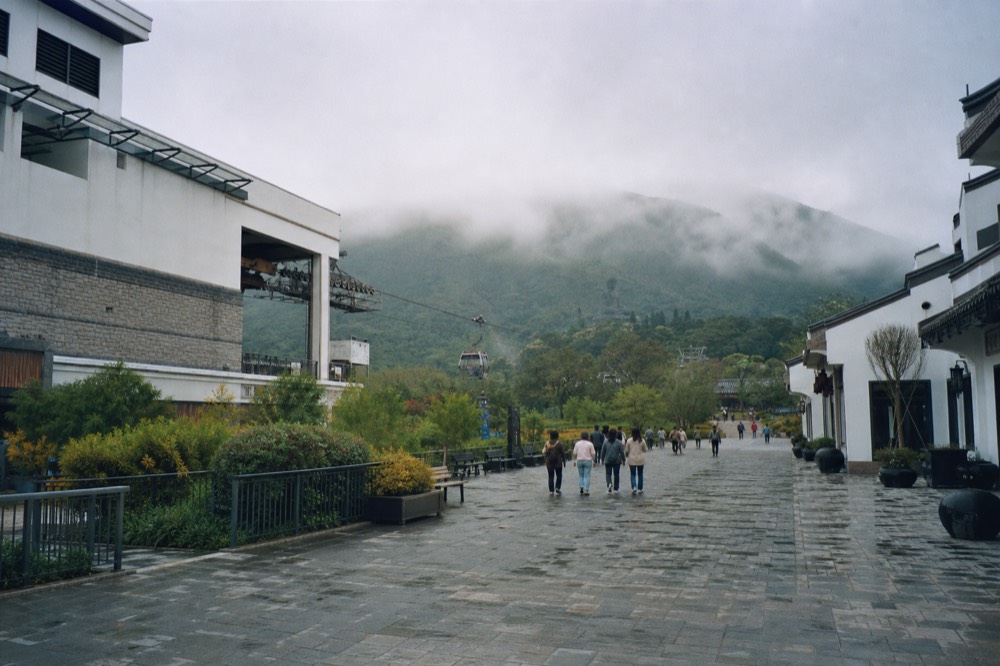 The Ngong Ping plaza and path towards the Big Buddha with visitors walking, distant hills, no text, no logos, no people