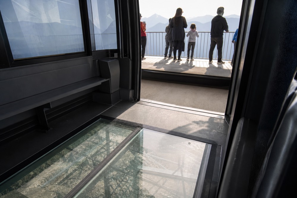 Interior of a cable car cabin showing a transparent glass floor panel above the terrain, no text, no logos, no people.