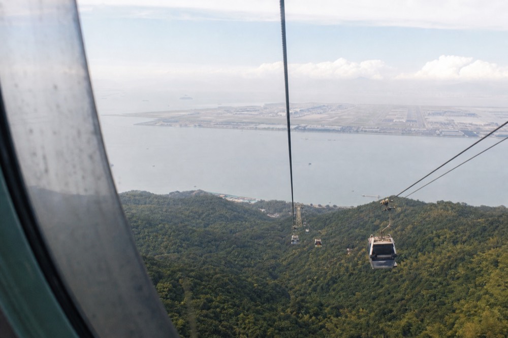 A view from a high cable car over green slopes, sea and airport infrastructure on a clear day, no text, no logos, no people.