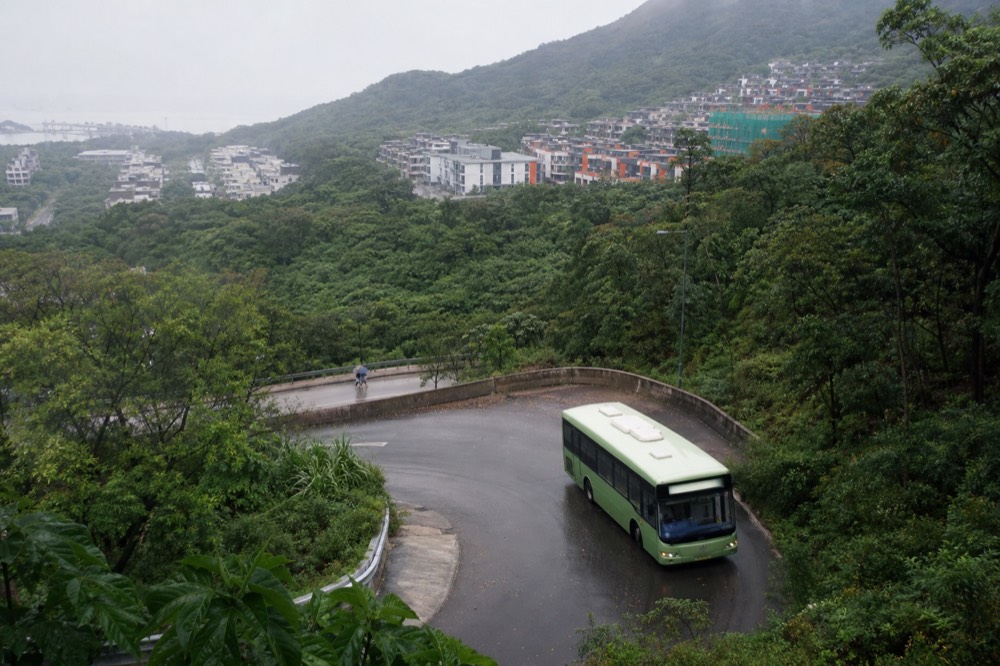 Green single-decker bus on a winding mountain road on Lantau, no text, no logos, no people