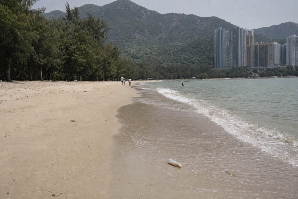 Wide sandy beach with gentle waves and wooded hills behind, no text, no logos, no people