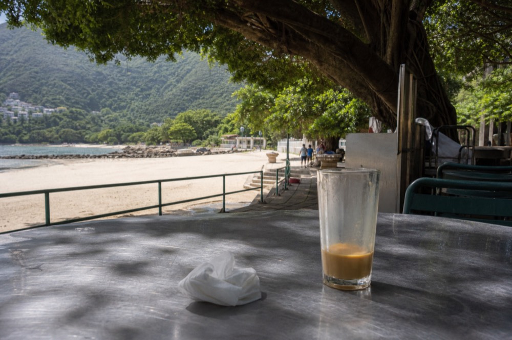 Beachside eating spot with tables near the sand under trees, no text, no logos, no people