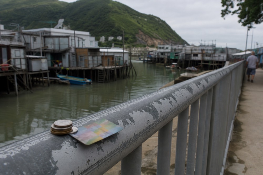 Coins and an Octopus card on a bus stop bench at Tai O, no text, no logos, no people.