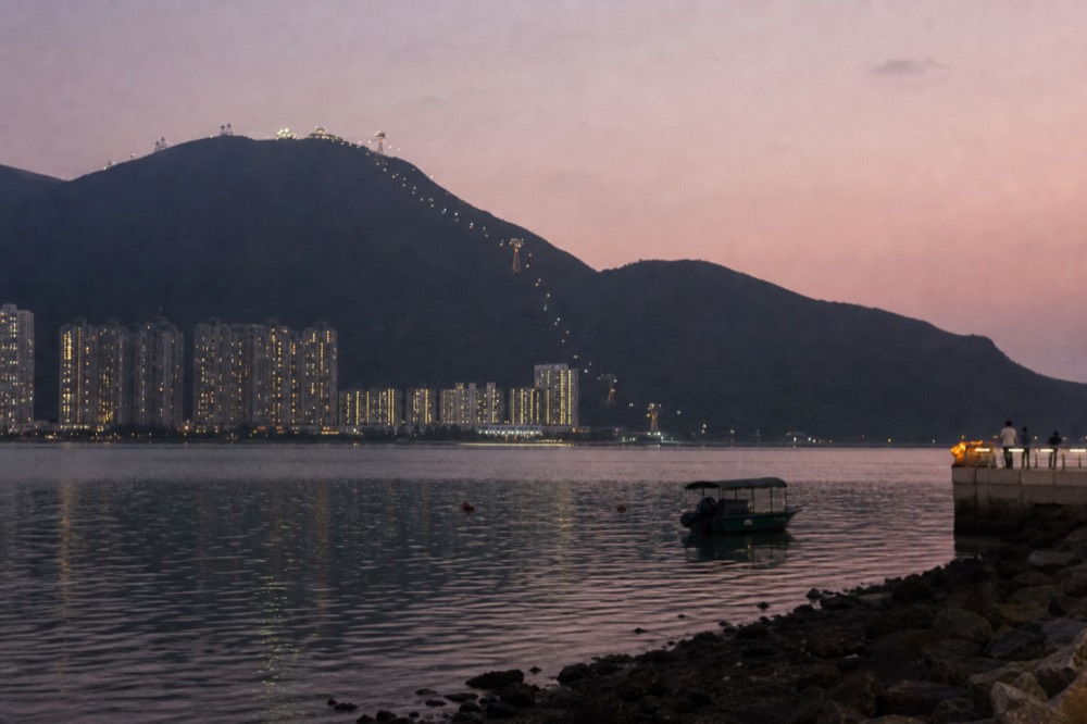 Evening view across Tung Chung Bay with the cable car line visible on the hillside, no text, no logos, no people.