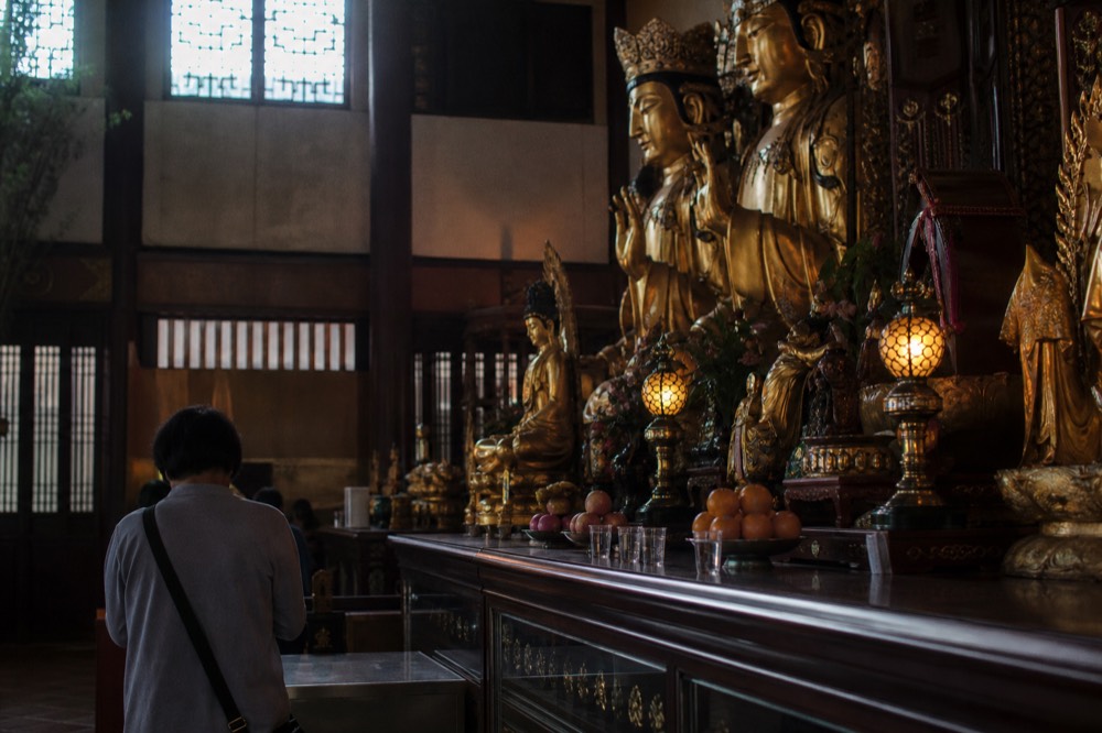 Golden Buddha statues and offerings inside a dimly lit shrine hall, no text, no logos, no people