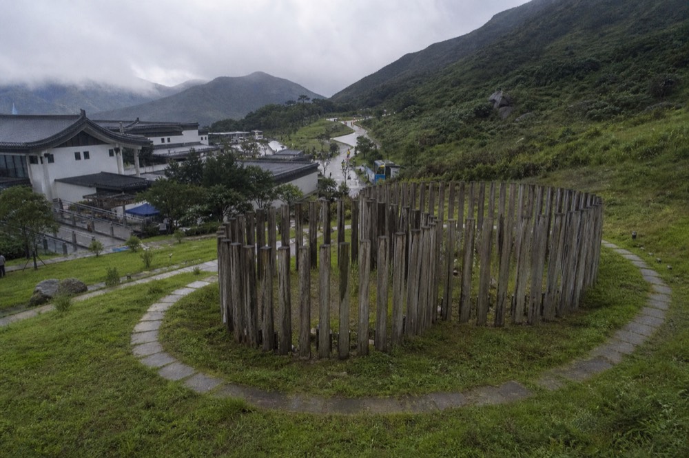 Timber columns of the Wisdom Path arranged on a green hillside below Lantau Peak, no text, no logos, no people